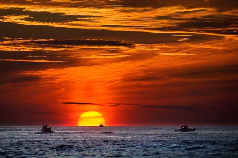 The sun rises over fishing boats in the Atlantic Ocean, Sept. 8, 2022, off of Kennebunkport, Maine.
