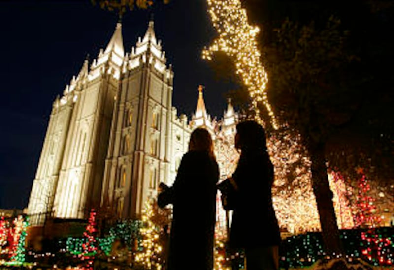 Sister missionaries stand and look at the temple amidst the Christmas lights on Temple Square on Nov
