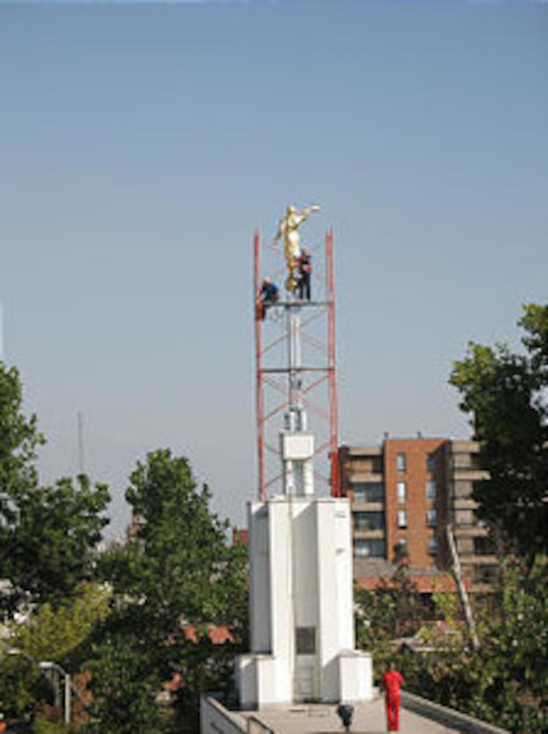 Workers attach a new trumpet to the angel statue atop the Santiago temple after the earthquake destr