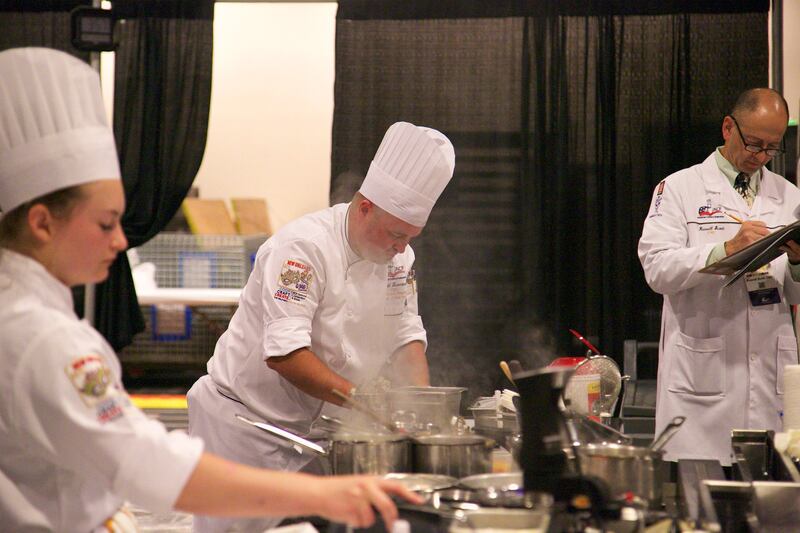 A judge takes notes as Chef Todd Leonard prepares a four-course meal at the 2018 National Chef of the Year competition in New Orleans.