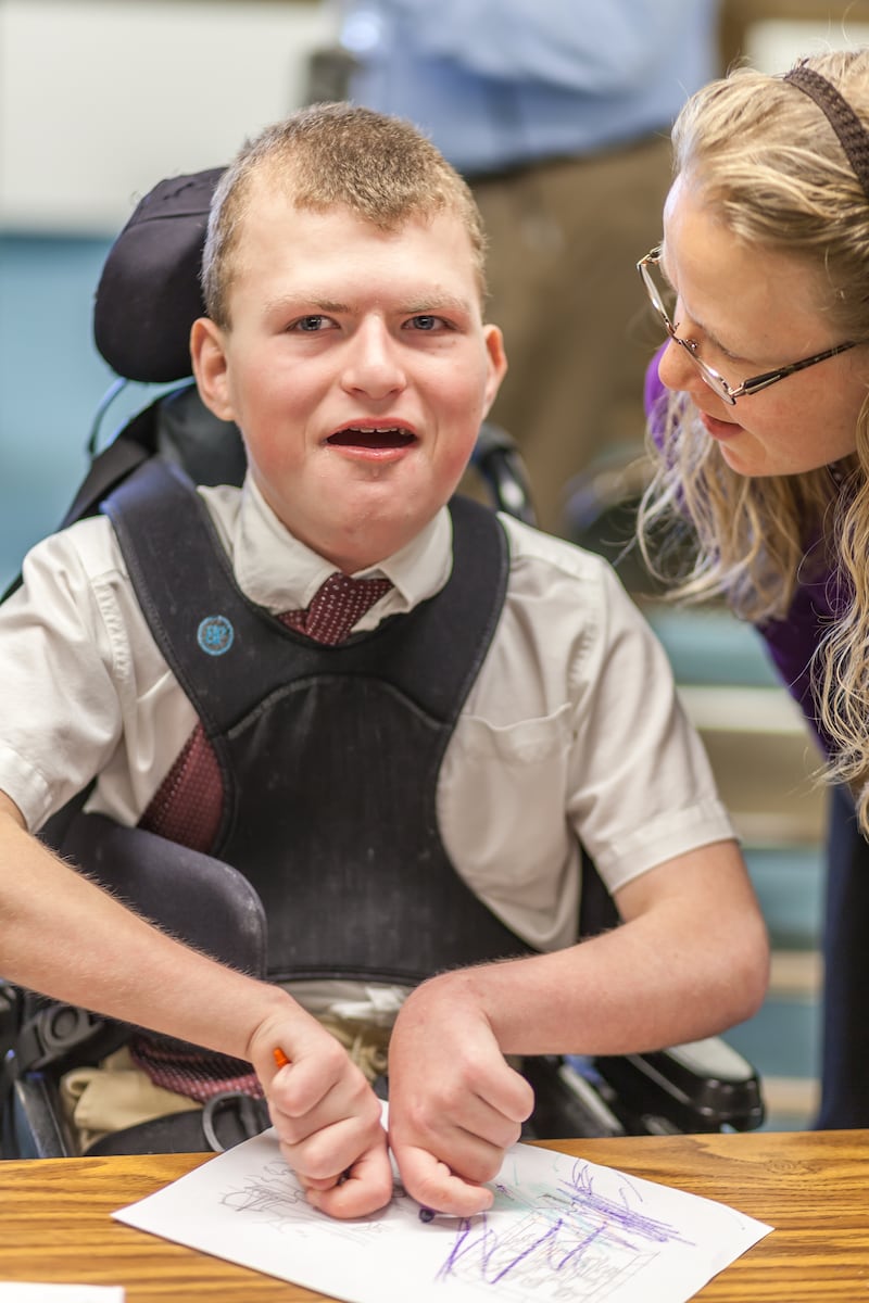 A young man in a wheelchair colors a picture.