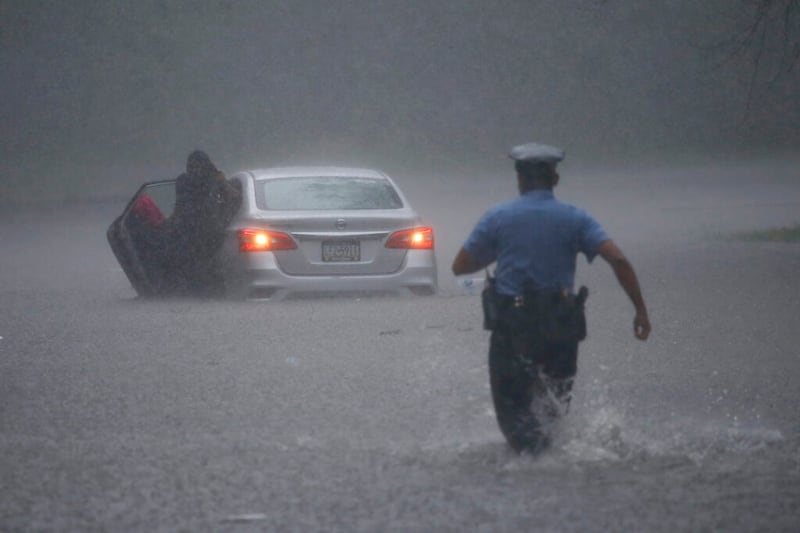 A Philadelphia police officer rushes to help a stranded motorist during Tropical Storm Isaias, Tuesday, Aug. 4, 2020, in Philadelphia. The storm spawned tornadoes and dumped rain during an inland march up the U.S. East Coast after making landfall as a hurricane along the North Carolina coast. (AP Photo/Matt Slocum)