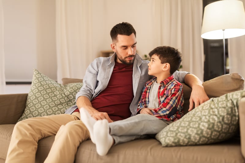 A father and son talk as they sit on a couch.