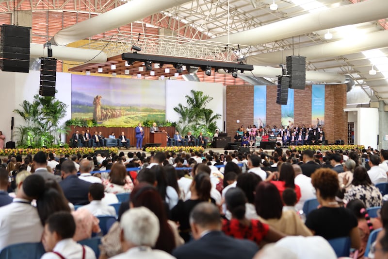 Elder Ronald A. Rasband of the Quorum of the Twelve Apostles stands at the pulpit and speaks to members with the help of a translator during a special conference in Santiago de los Caballeros, Dominican Republic, on Sept. 13, 2026.