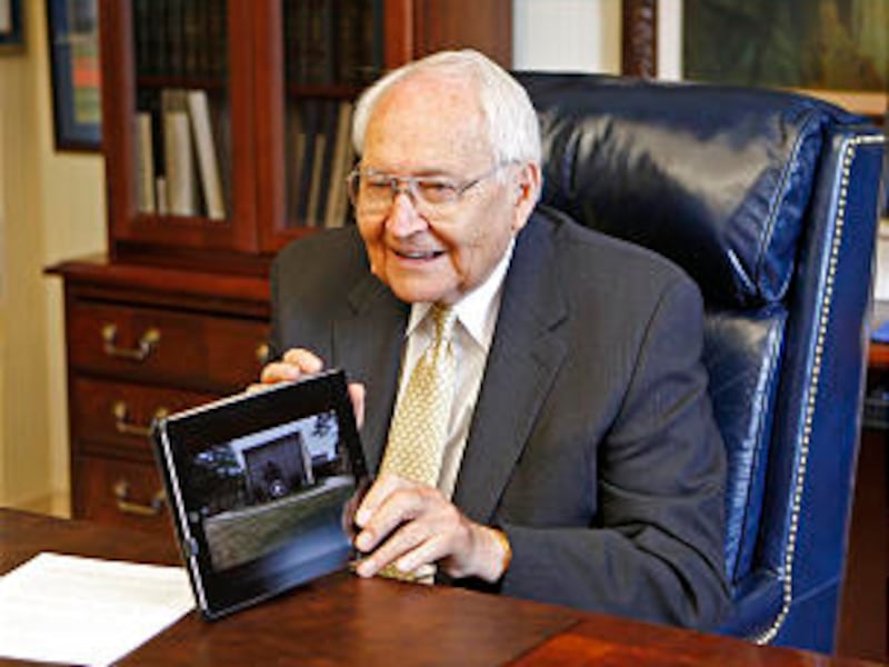 Elder L. Tom Perry sits at his desk and shows some of the photos he has taken while traveling this s