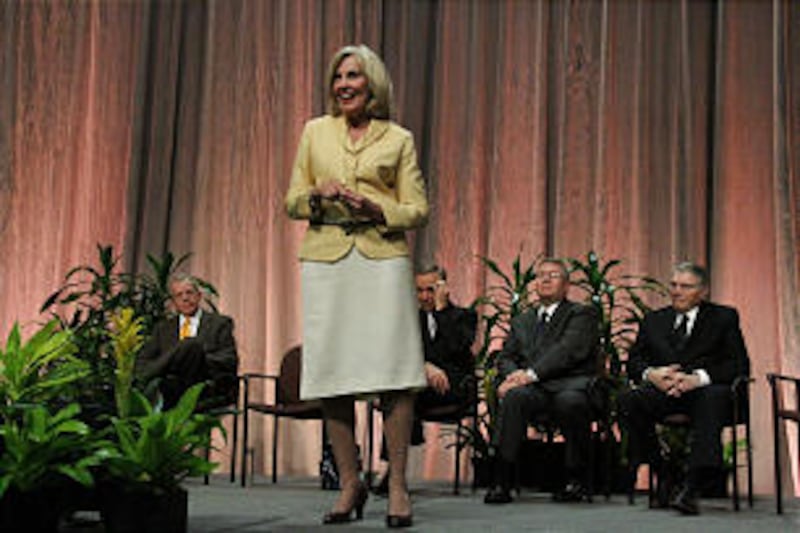 Sister Dalton speaks to audience; seated on the stage behind her are her husband, Stephen E. Dalton,