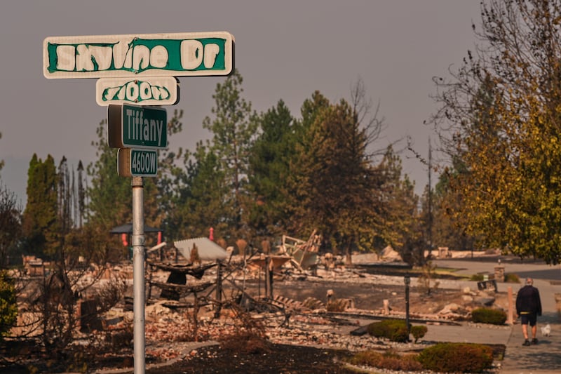 A street sign shows sign of fire damage as a person walks their dog after a wildfire hit the northern part of Spokane, Washington, Monday, Aug. 3, 2026.