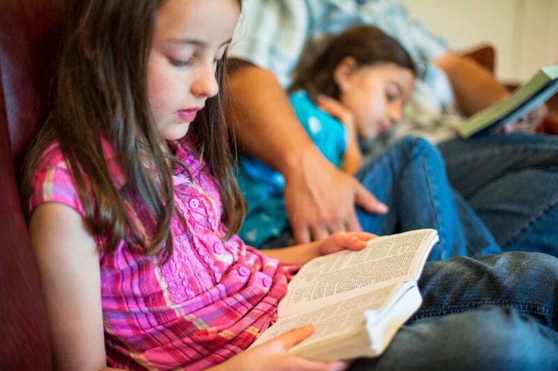A young girl reads from the scriptures with her family. In 2026, Latter-day Saints will study the Old Testament with “Come, Follow Me.”