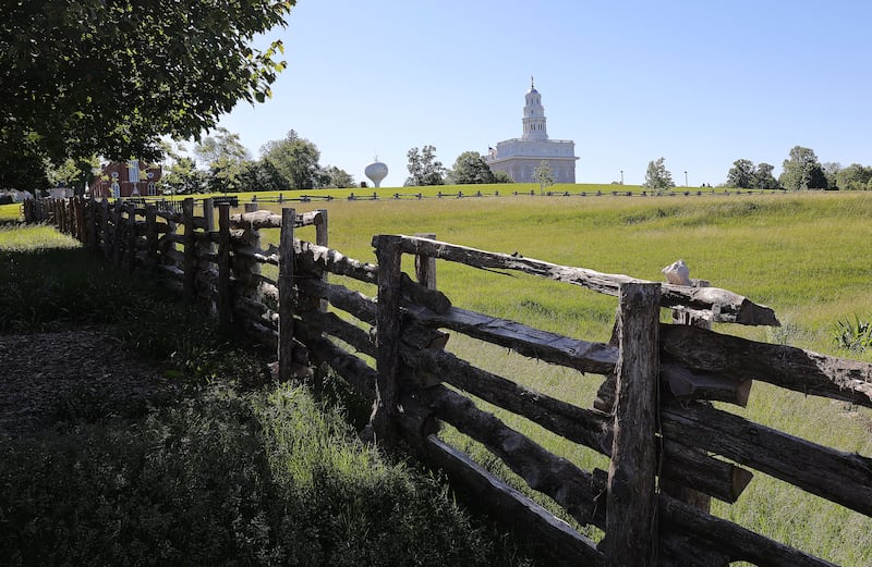 White, single spire rebuilt Nauvoo Illinois Temple is seen from across a fence in the front and a field.