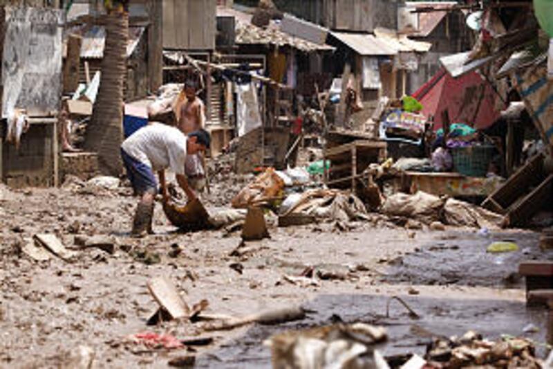 Residents remove debris in a mud-covered residential area of Manila. Evacuees slowly return to their