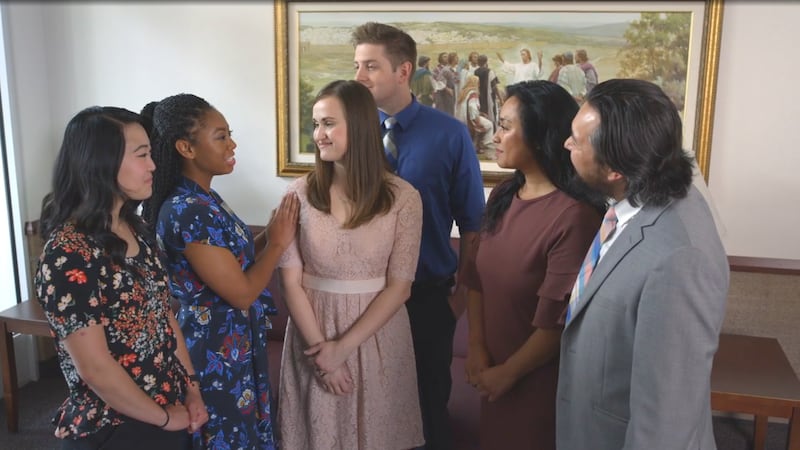 Six people greet each other in the foyer of a Church building before sacrament meeting.