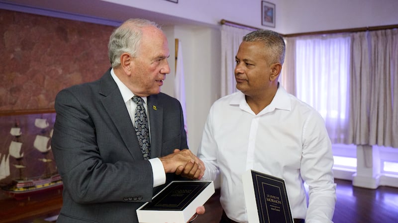 Elder Ronald A. Rasband shakes hands with Sebastien Pillay, the vice president of Seychelles, as they hold copies of the Book of Mormon on Oct. 29, 2025.