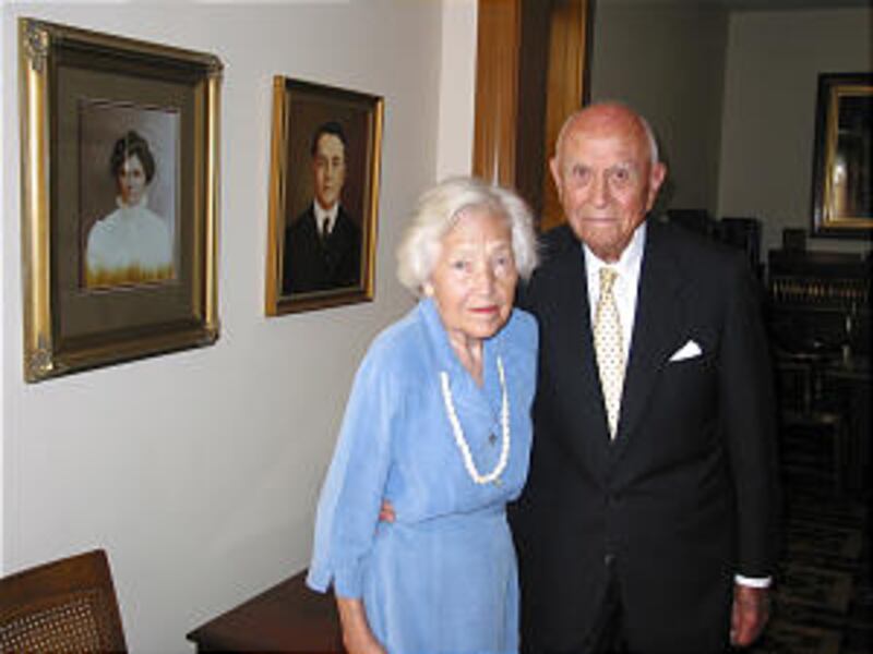 Elder David B. Haight and wife, Ruby, standing in parlor of old home in Oakley, Idaho. Portraits on