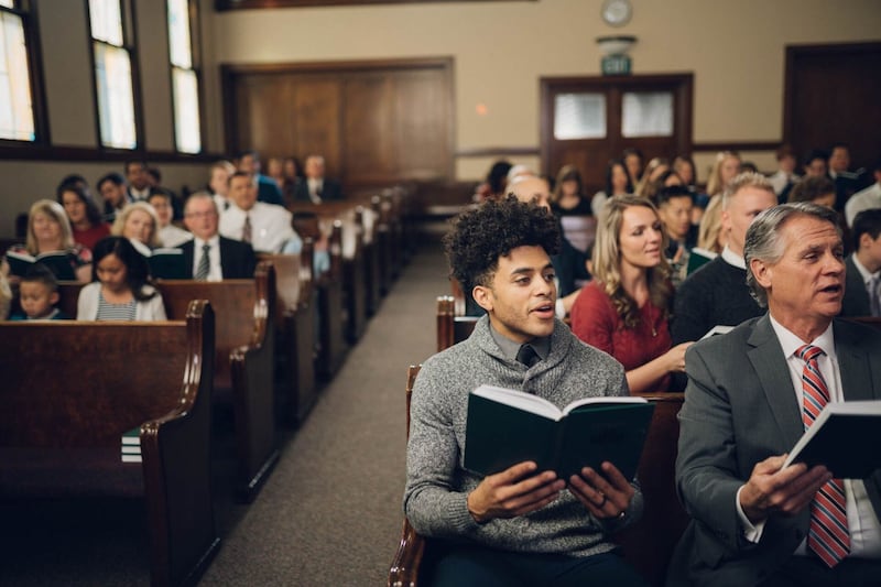 People sit in church pews and sing as a congregation.