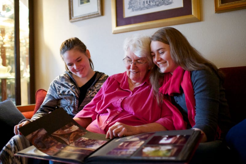 Two young women sit with their grandmother and look at family photographs.