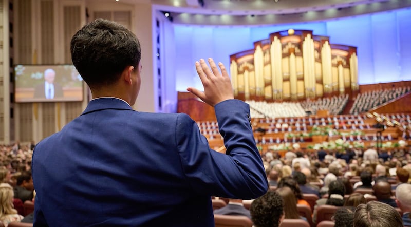 A young man is photographed while raising his hand during general conference in the Conference Center in Salt Lake City, Utah.